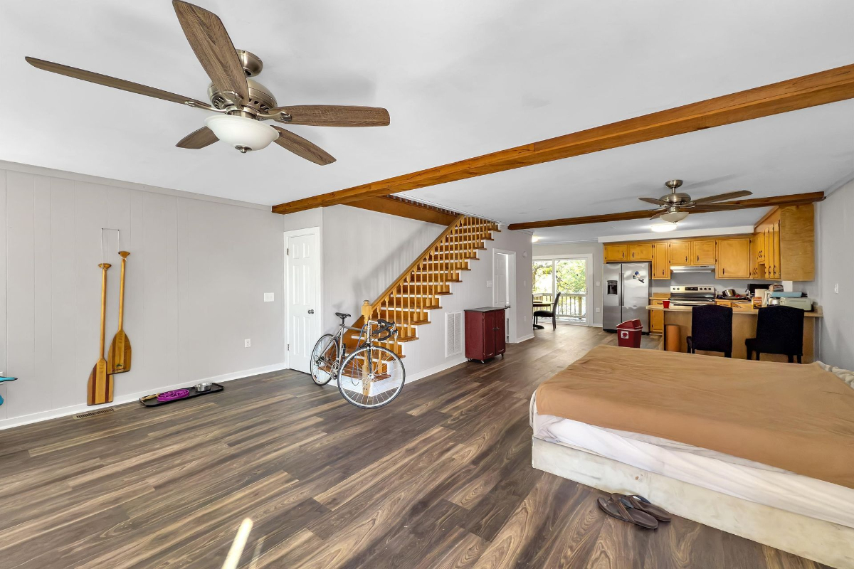 Open-concept living space includes warm wood accents, a functional staircase, and an adjoining kitchen with natural cabinetry.