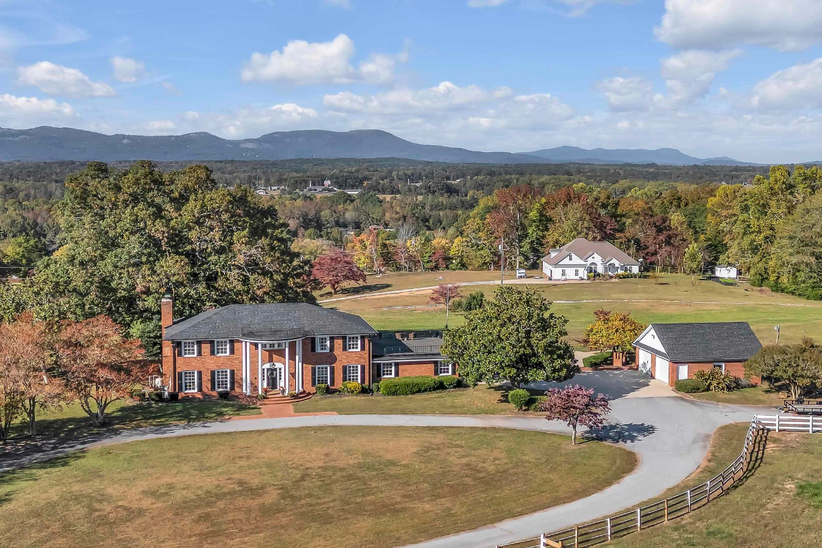 Sprawling countryside estate featuring a stately brick home, detached garage, and expansive views of rolling hills and mountains.