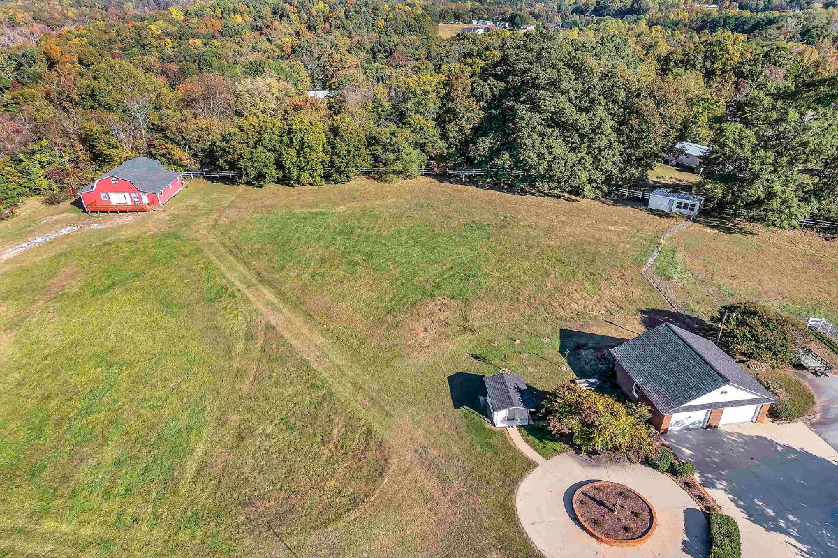 A vibrant red barn anchors a picturesque property surrounded by sprawling green pastures and natural wooded areas.