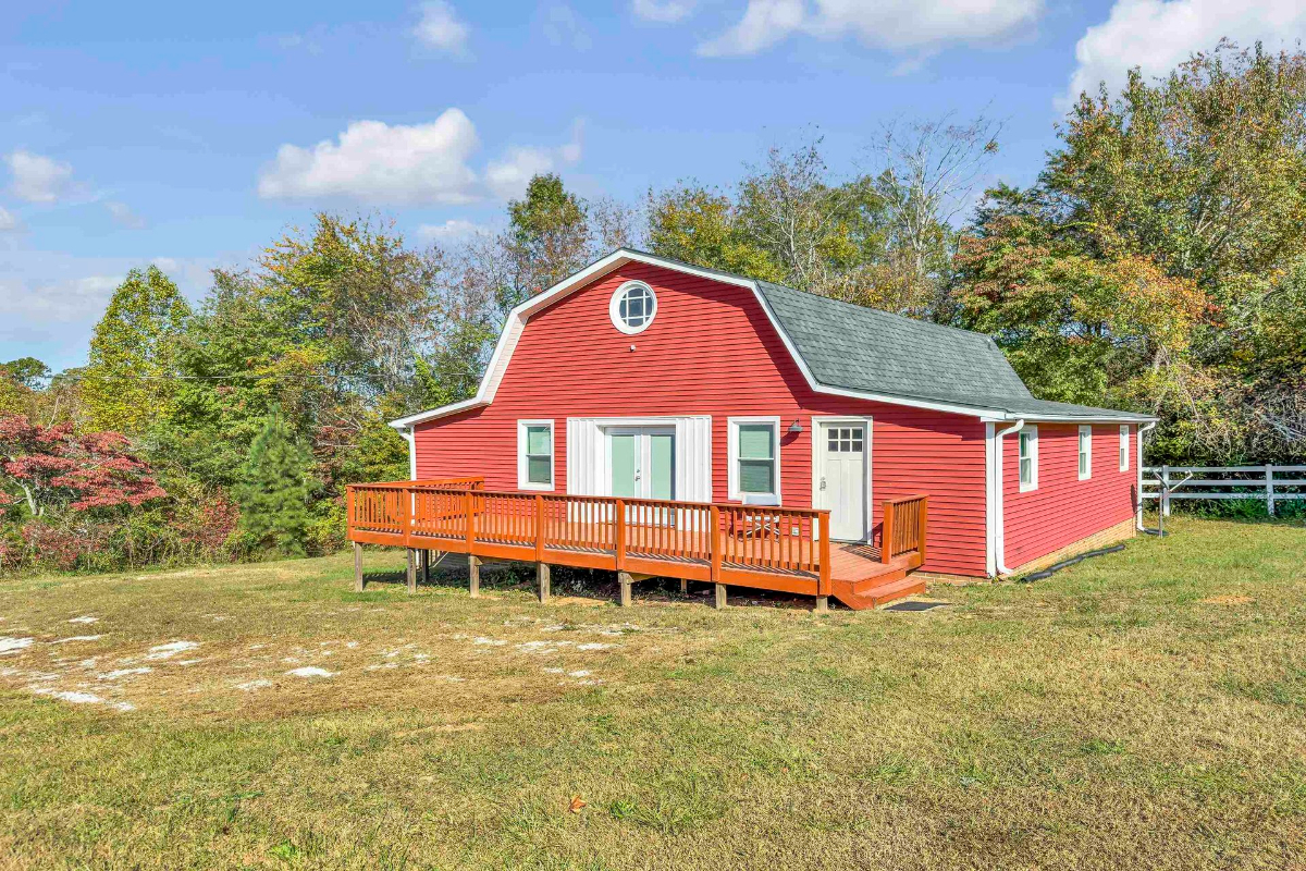 A bright red barn-style structure with a spacious wooden deck stands against a backdrop of lush trees and open greenery.