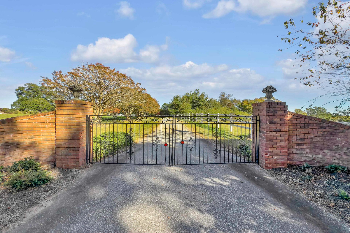 Grand gated entrance adorned with brick pillars, leading to a picturesque estate surrounded by lush greenery.