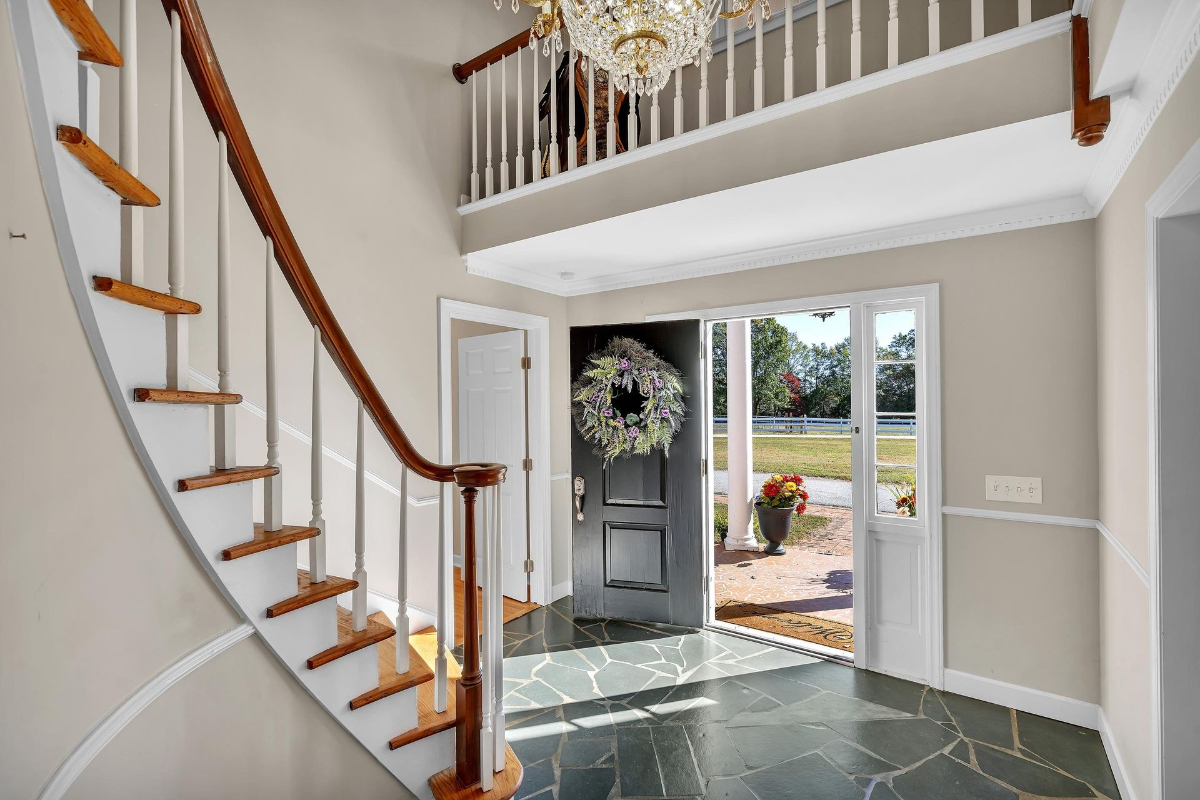 Elegant foyer featuring a curved staircase with rich wooden accents, slate tile flooring, and a grand chandelier.