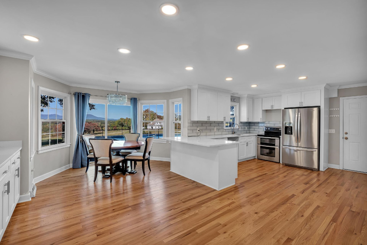 The open kitchen showcases sleek white cabinetry, stainless steel appliances, and a breakfast nook with expansive views of the pool and mountains.