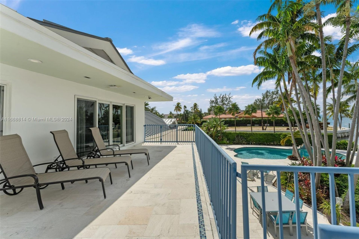 Spacious balcony with lounge chairs overlooking a pool and lush tropical landscaping.