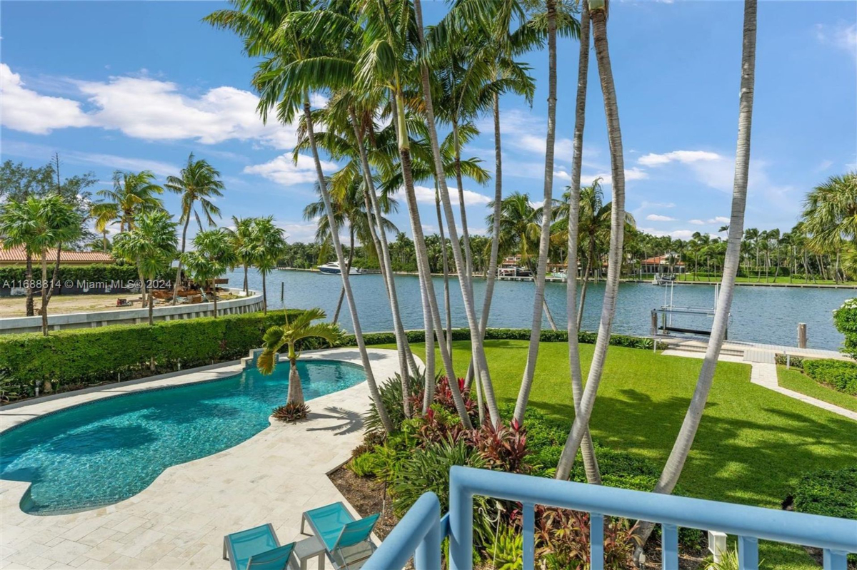 Lush tropical grounds featuring a lagoon-style pool and waterfront views framed by tall palm trees.