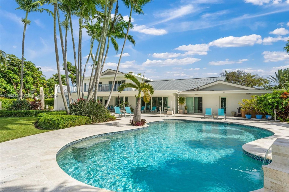 Luxurious poolside area with lush greenery, towering palm trees, and a contemporary residence in the background.