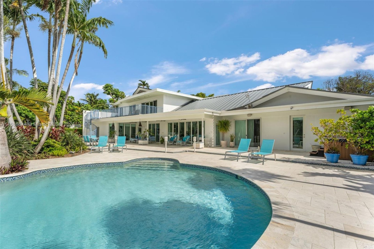 Poolside view of a contemporary two-story home with expansive outdoor seating areas.