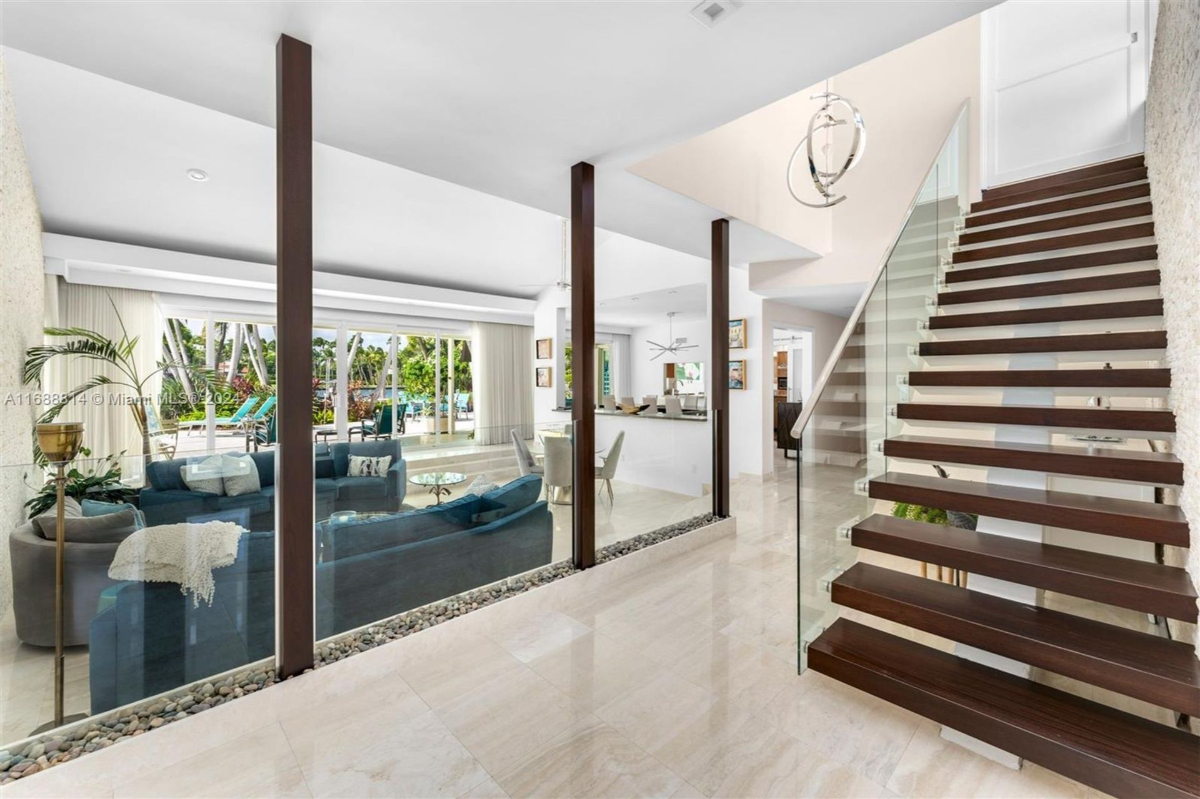 Open-plan interior with floating staircase and glass railing adjacent to a bright living area.