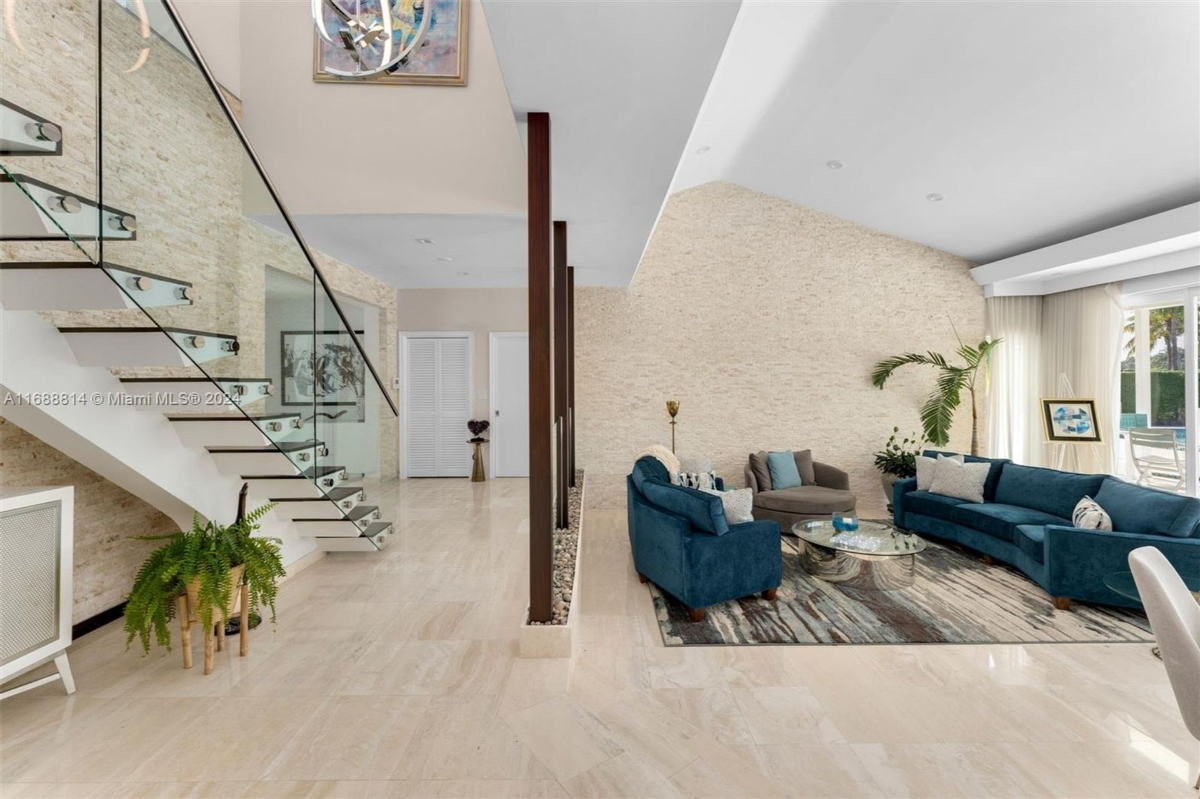 Spacious living area with modern staircase, glass railings, and textured accent walls.