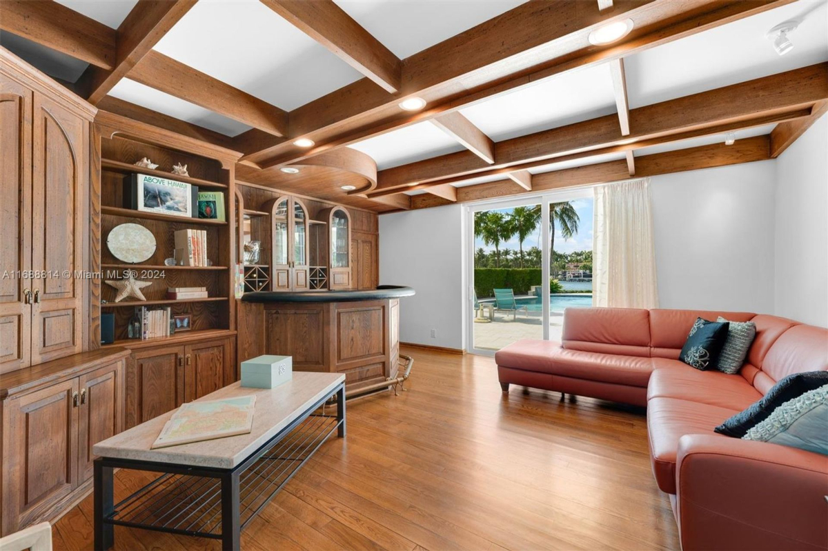 Wood-paneled lounge with built-in shelving, coffered ceiling, and poolside views.