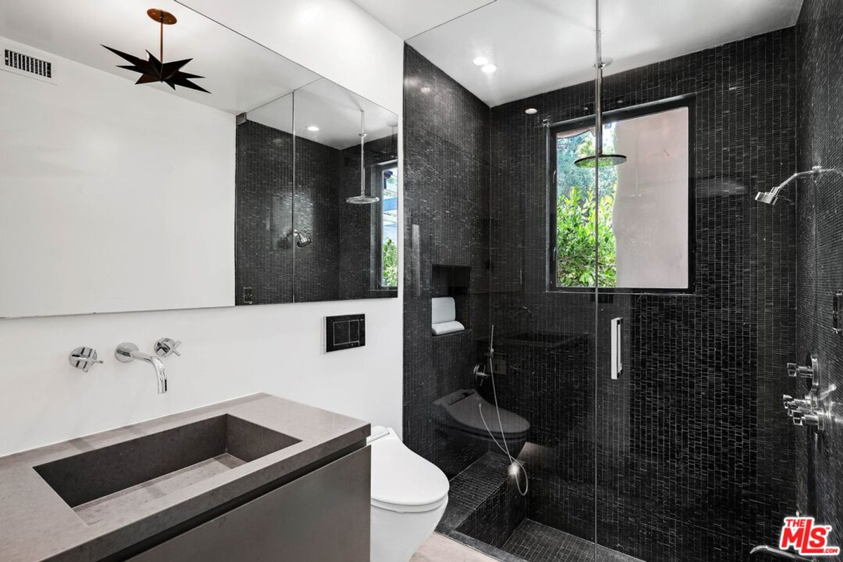 Modern bathroom featuring sleek black tile, a walk-in shower, and a large mirrored vanity.