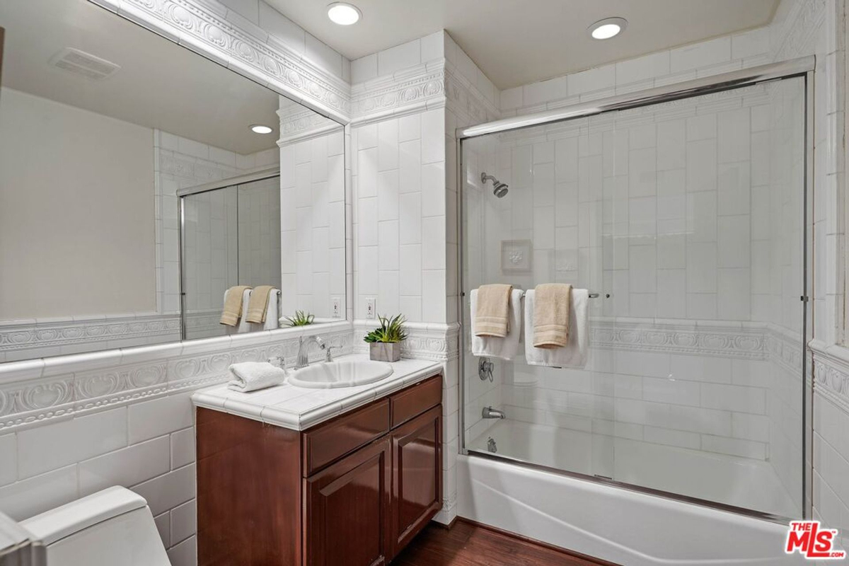 Bright bathroom with classic white tile, a mirrored vanity, and a glass-enclosed tub.