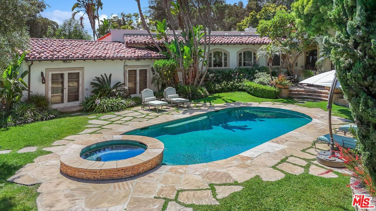 A serene pool and spa area is surrounded by lush landscaping and a stone patio.