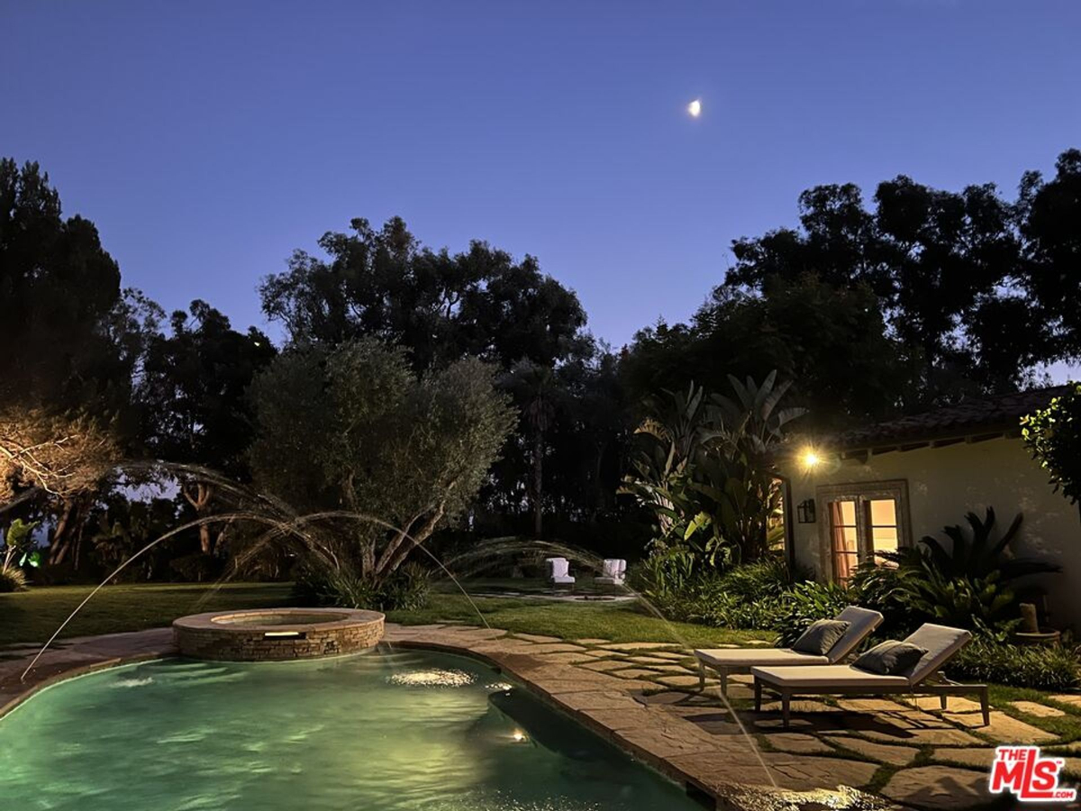 The poolside glows under soft moonlight and garden illumination.