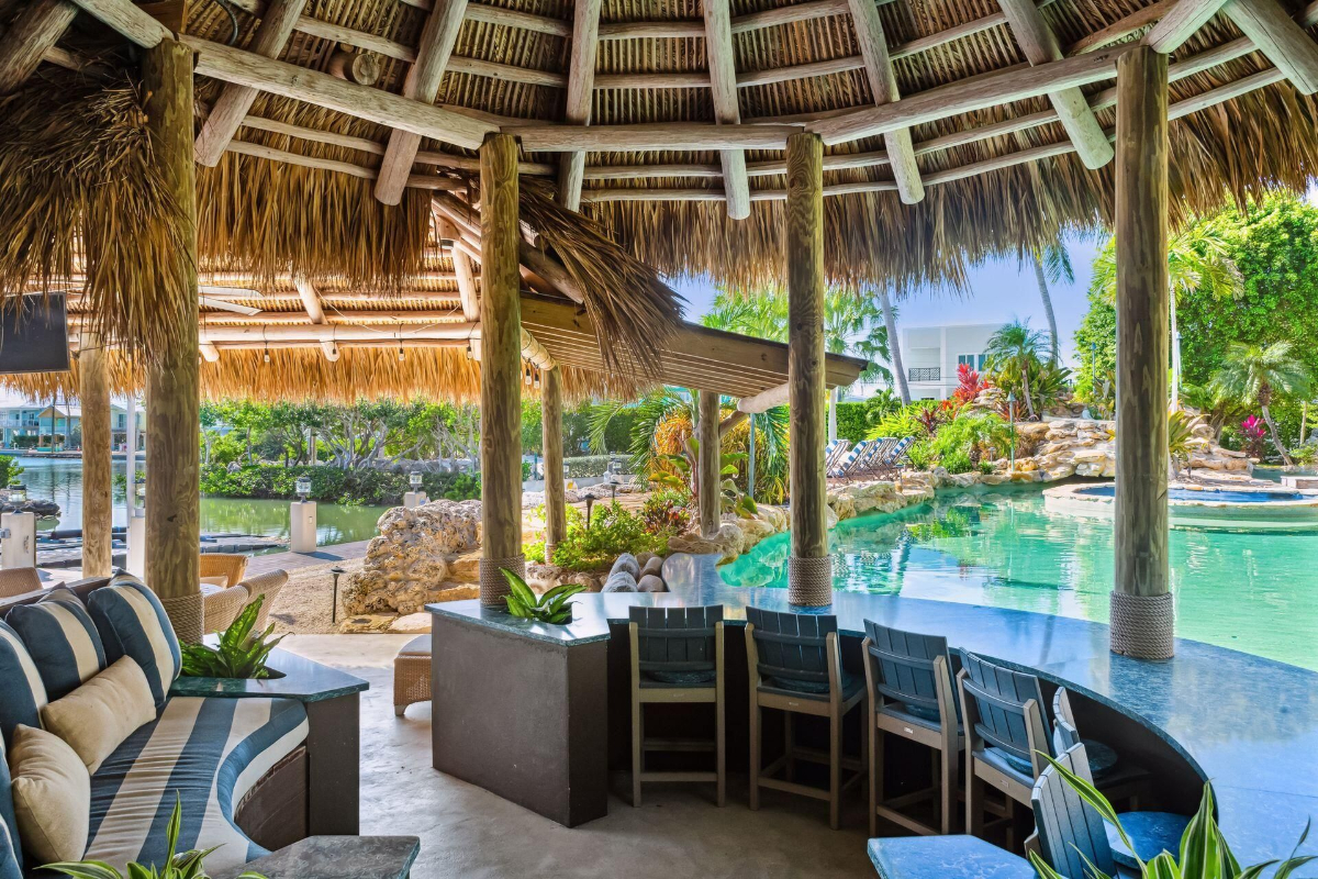 Open tiki hut overlooks a lagoon-style pool and lush tropical landscaping, perfect for relaxation.