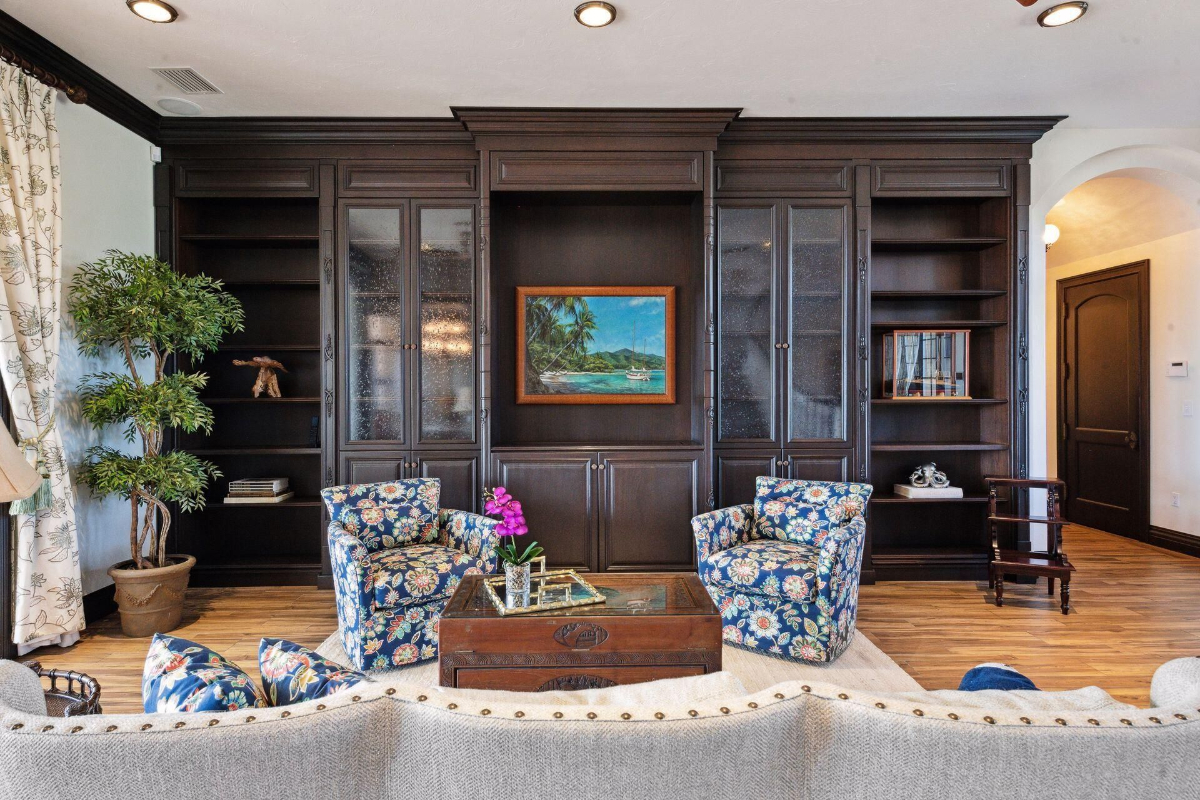 A beautifully arranged seating area showcases floral armchairs, a centerpiece table with intricate carvings, and built-in dark wood cabinetry framing a serene landscape painting.