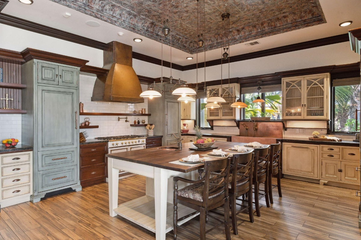 Gourmet kitchen blends vintage charm with modern luxury, featuring a copper range hood, intricate coffered ceiling, and spacious island seating.