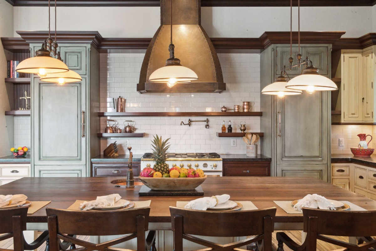 Kitchen combines rustic charm with modern elegance, featuring a large wooden island, industrial pendant lighting, and pastel cabinets.