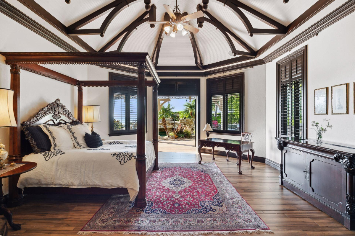 Bedroom features a dramatic vaulted ceiling, a carved four-poster bed, and stunning views of lush greenery through large windows.