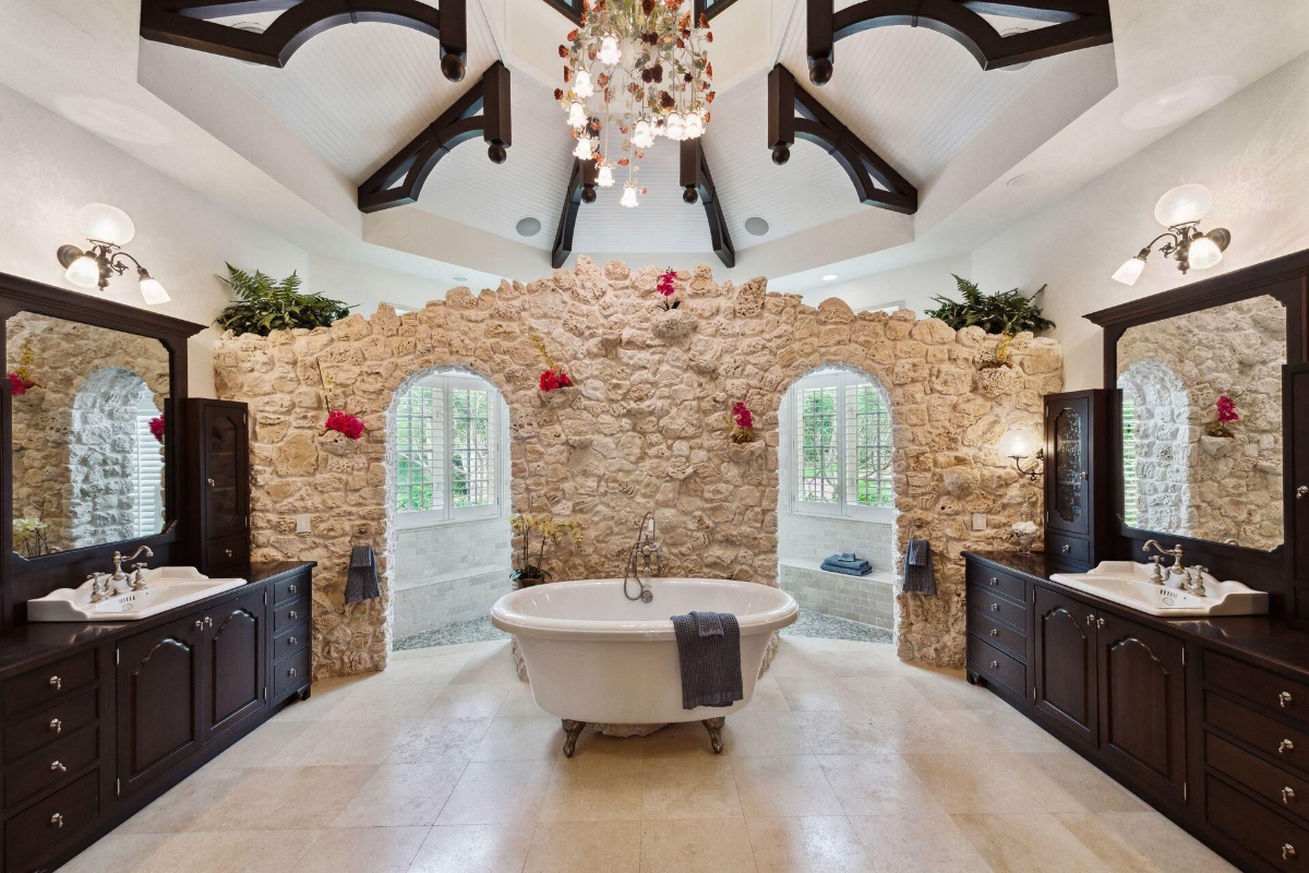 Bathroom boasts a freestanding clawfoot tub, stone accent walls, and vaulted ceilings with exposed beams for a spa-like ambiance.