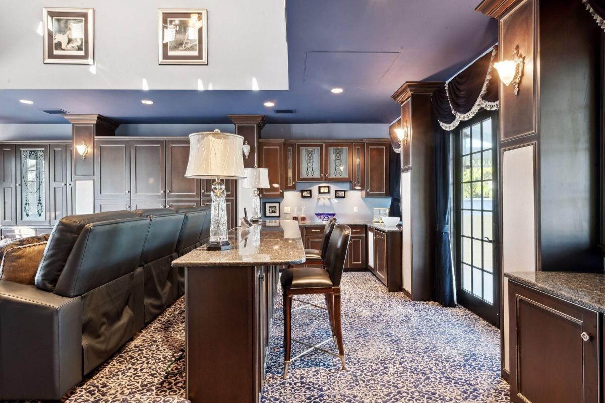 Home theater room boasts plush leather seating, a chic bar area with granite countertops, and custom cabinetry under a bold blue ceiling.