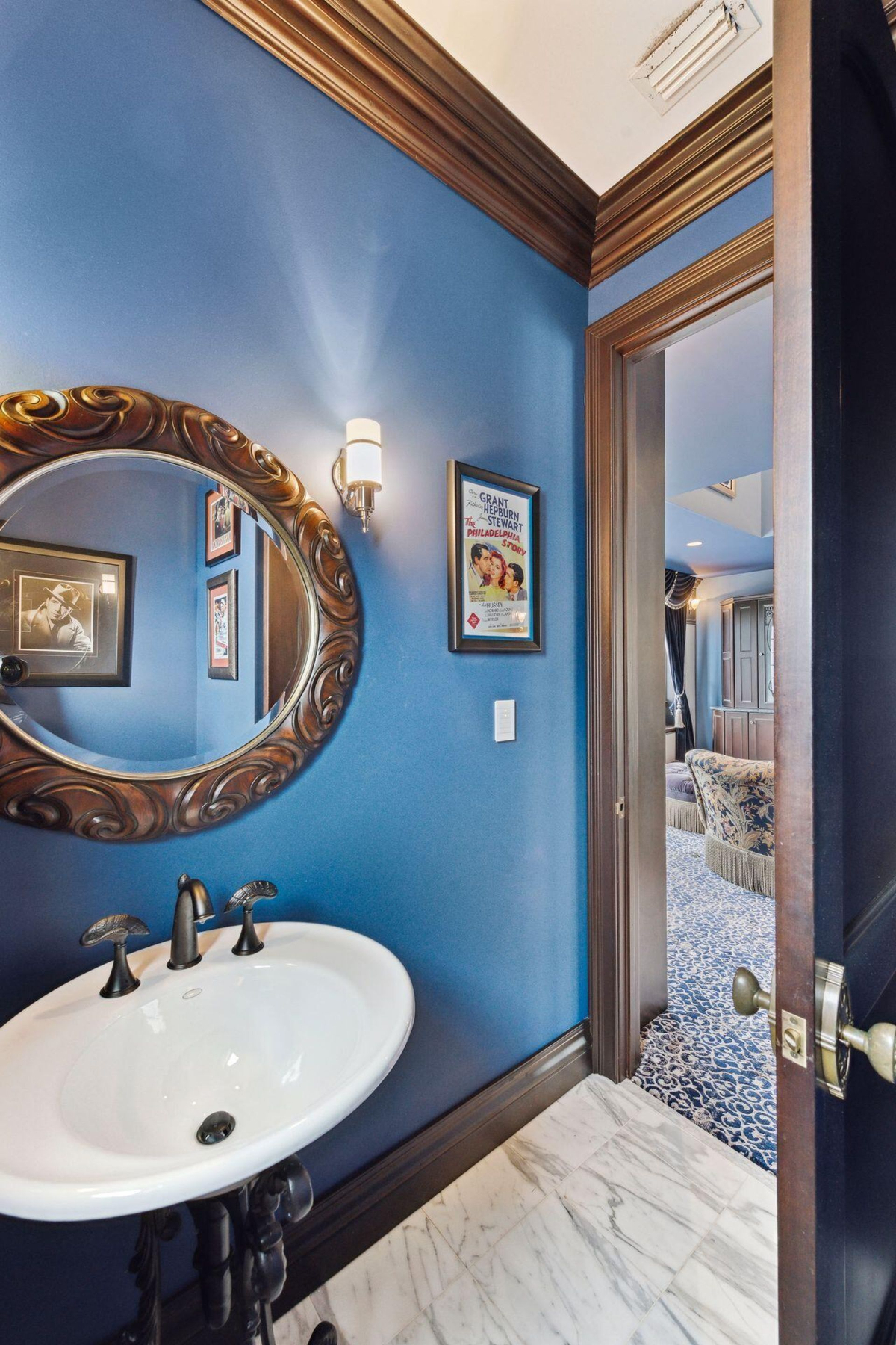 Powder room blends vintage charm with bold blue walls, accented by a decorative round mirror and classic lighting.