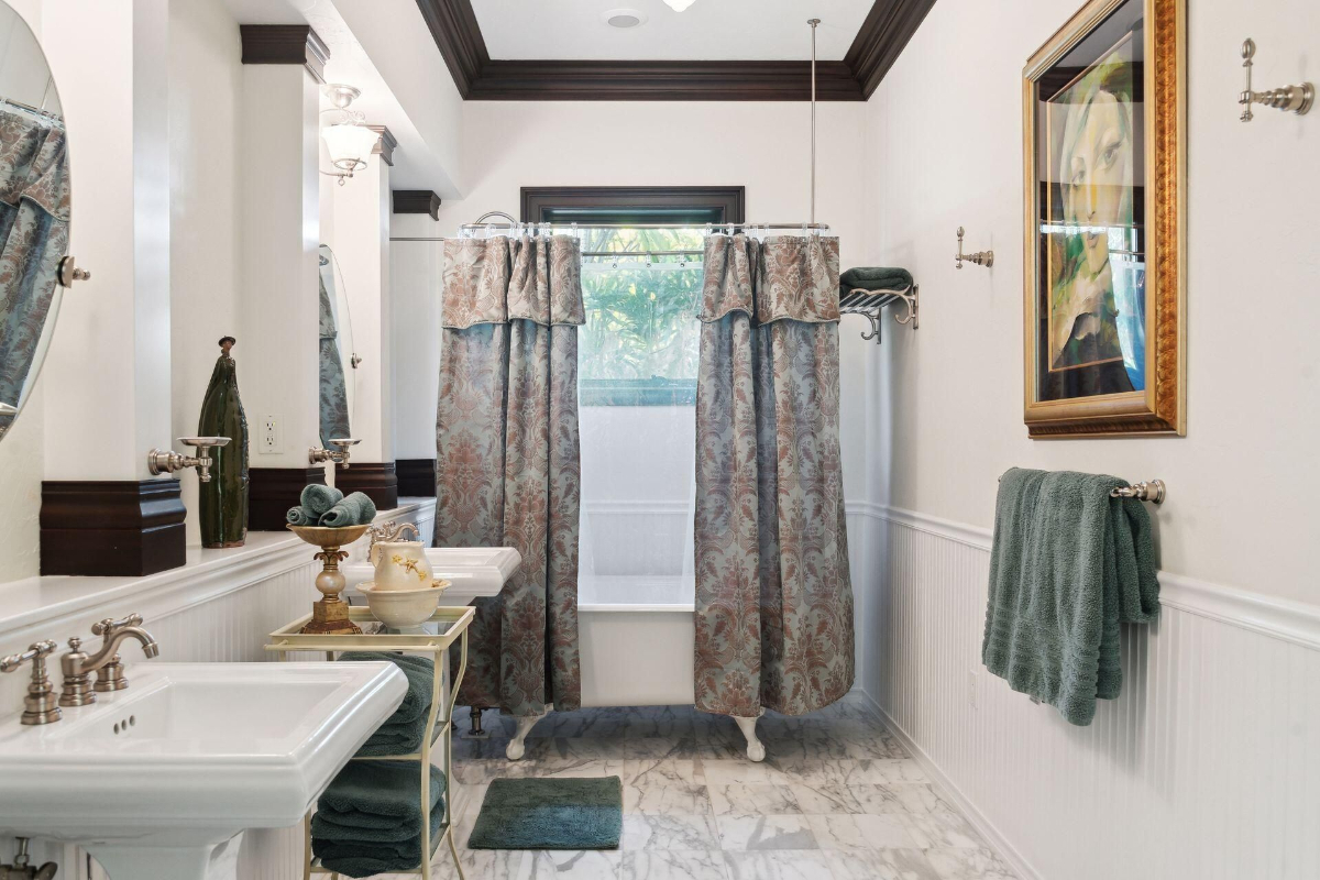 Bathroom features a clawfoot tub with floral curtains, pedestal sinks, and elegant marble flooring.