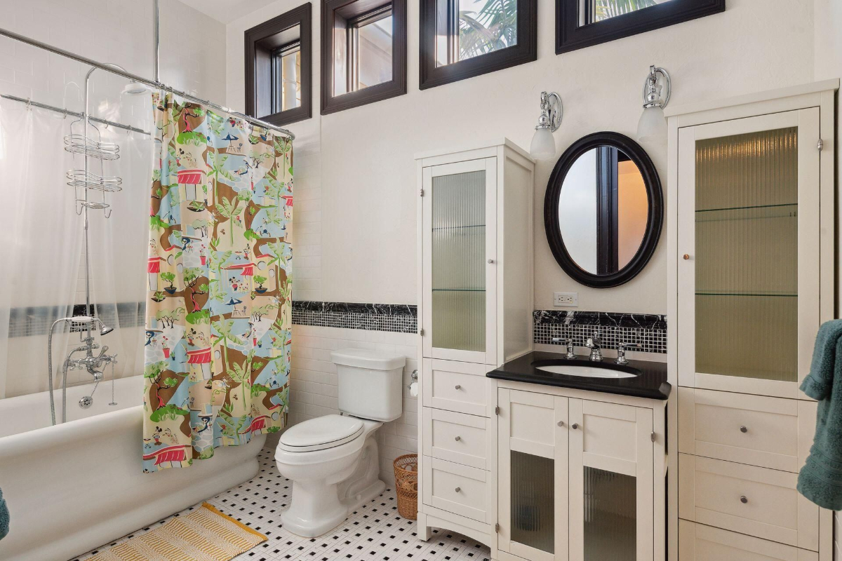 A bright and cheerful bathroom showcases playful animal-themed shower curtains, a black-and-white tiled floor, and charming cabinetry with glass accents.