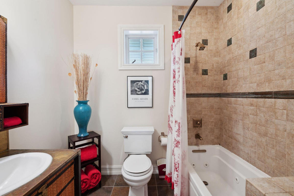 Bathroom features earth-toned tiles, a jetted bathtub, and pops of vibrant red accents.