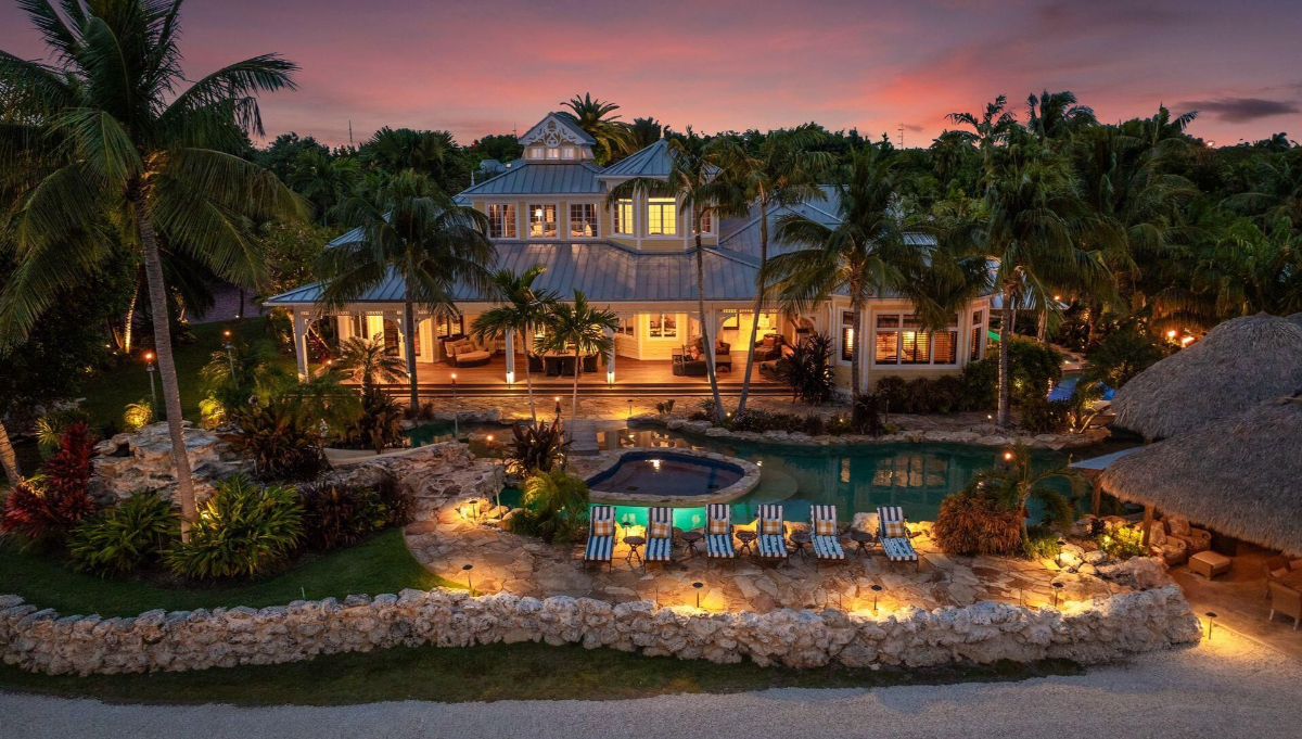 Tropical estate glows at dusk, showcasing a resort-style pool, spa, and lush landscaping framed by palm trees and ambient lighting.