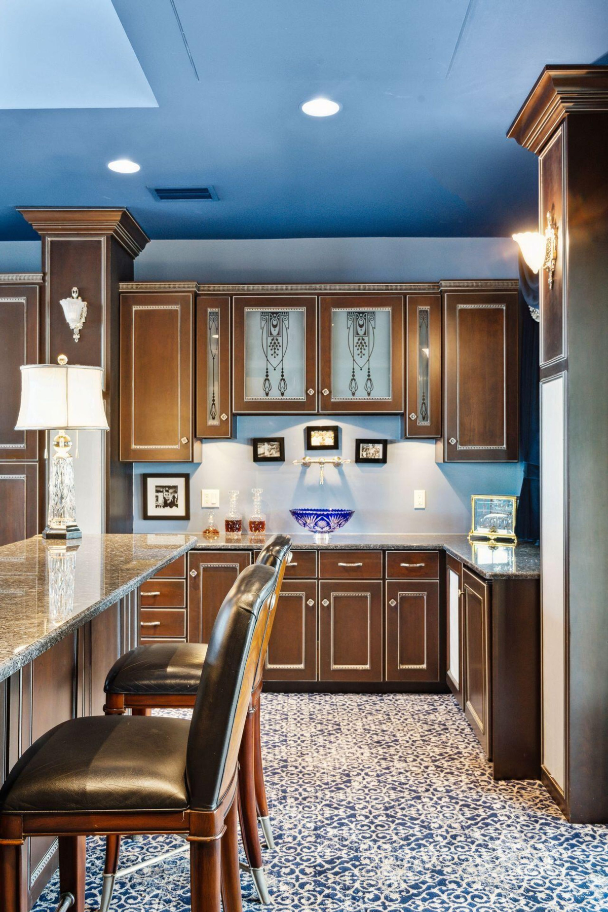 Bar area features custom cabinetry with intricate glass details, a polished granite countertop, and a bold patterned carpet adding a sophisticated touch.