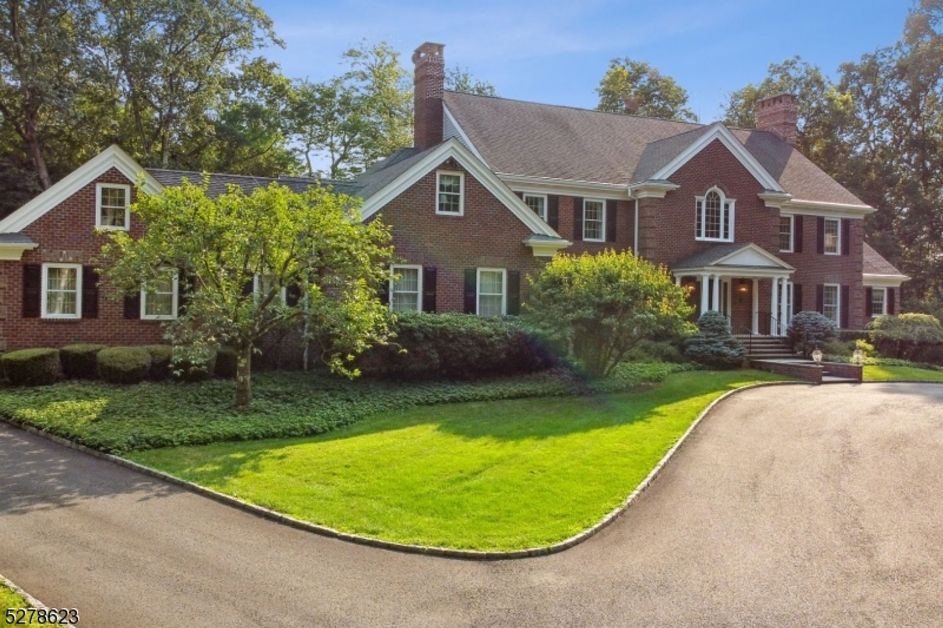 Classic brick estate surrounded by lush greenery and a circular driveway.