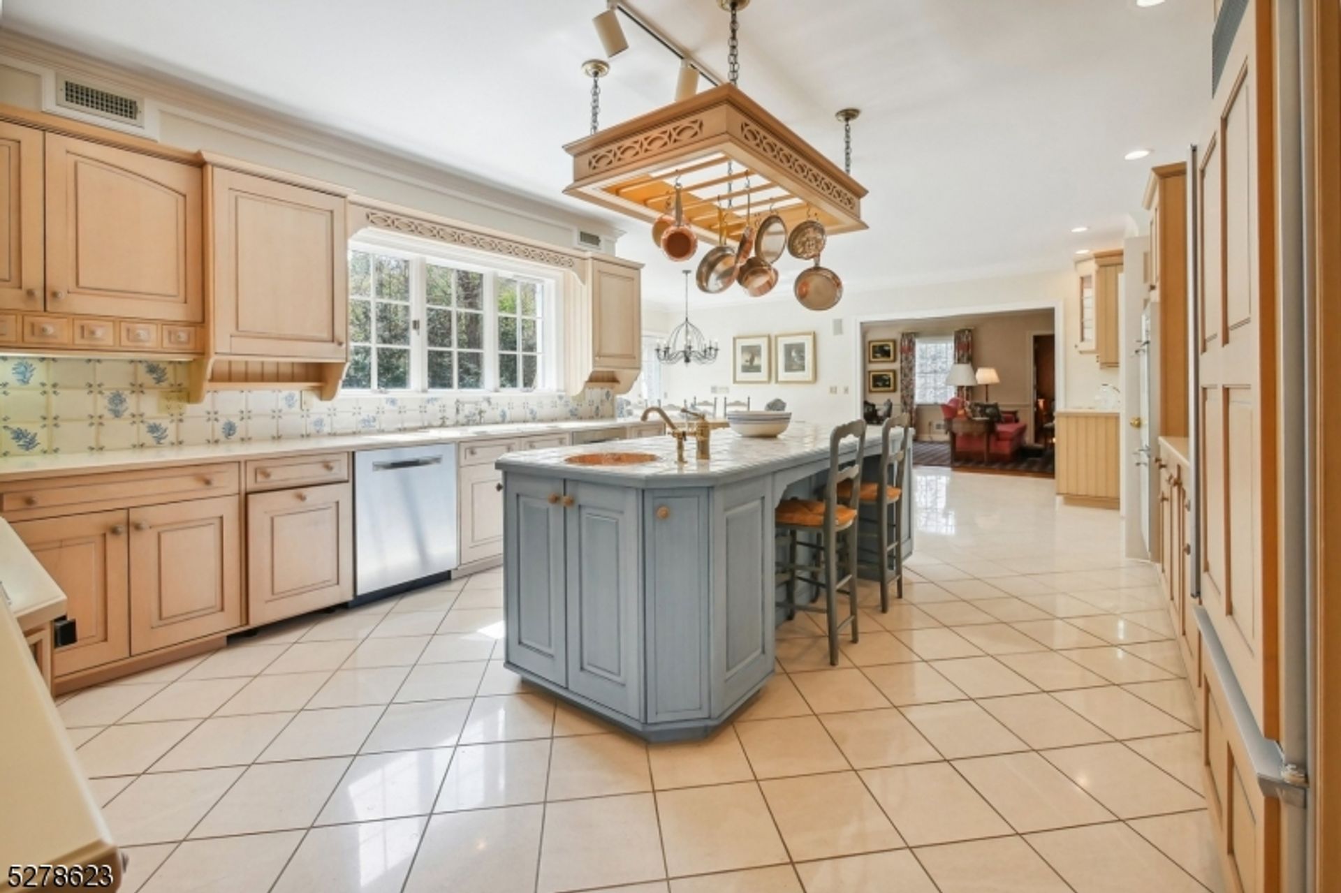 Charming kitchen with a pastel blue island, hanging pot rack, and large window overlooking the outdoors.