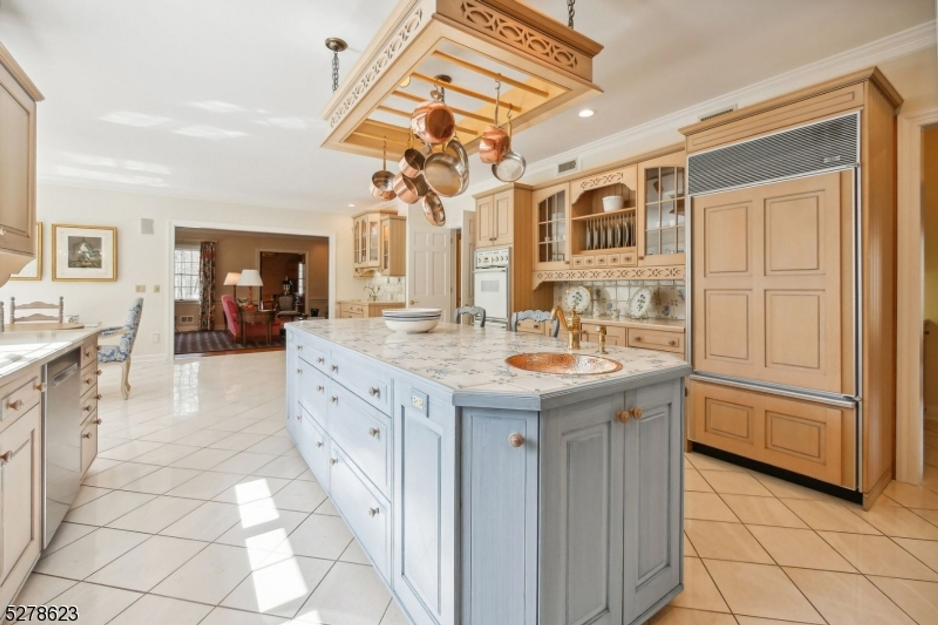 Elegant kitchen island with copper sink, detailed tile countertop, and overhead hanging copper pots.