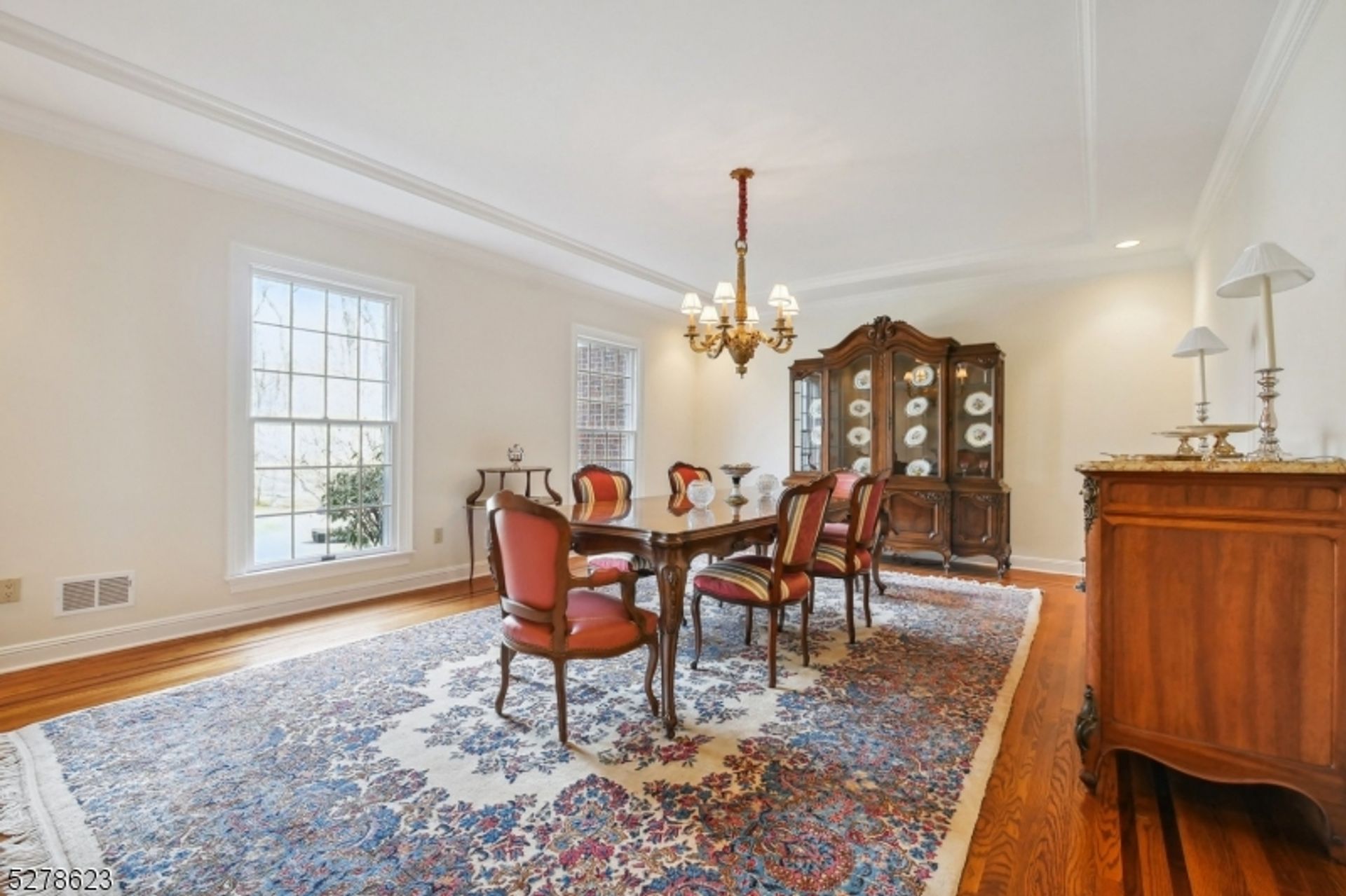 Refined dining area featuring ornate wooden furniture, vibrant area rug, and abundant natural light.