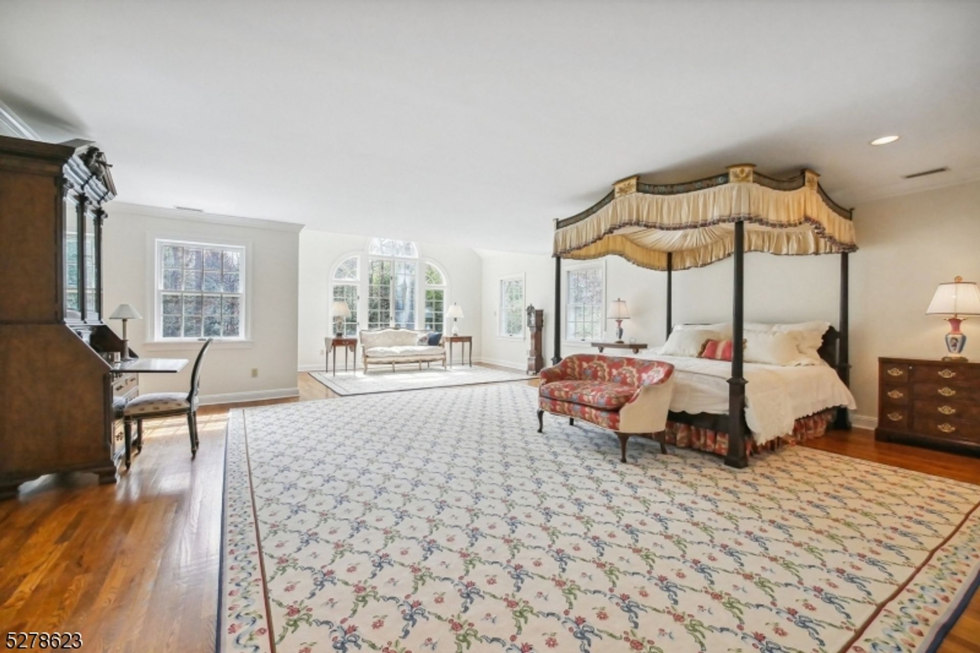 Grand bedroom suite features a four-poster canopy bed, elegant seating area, and abundant natural light from expansive windows.