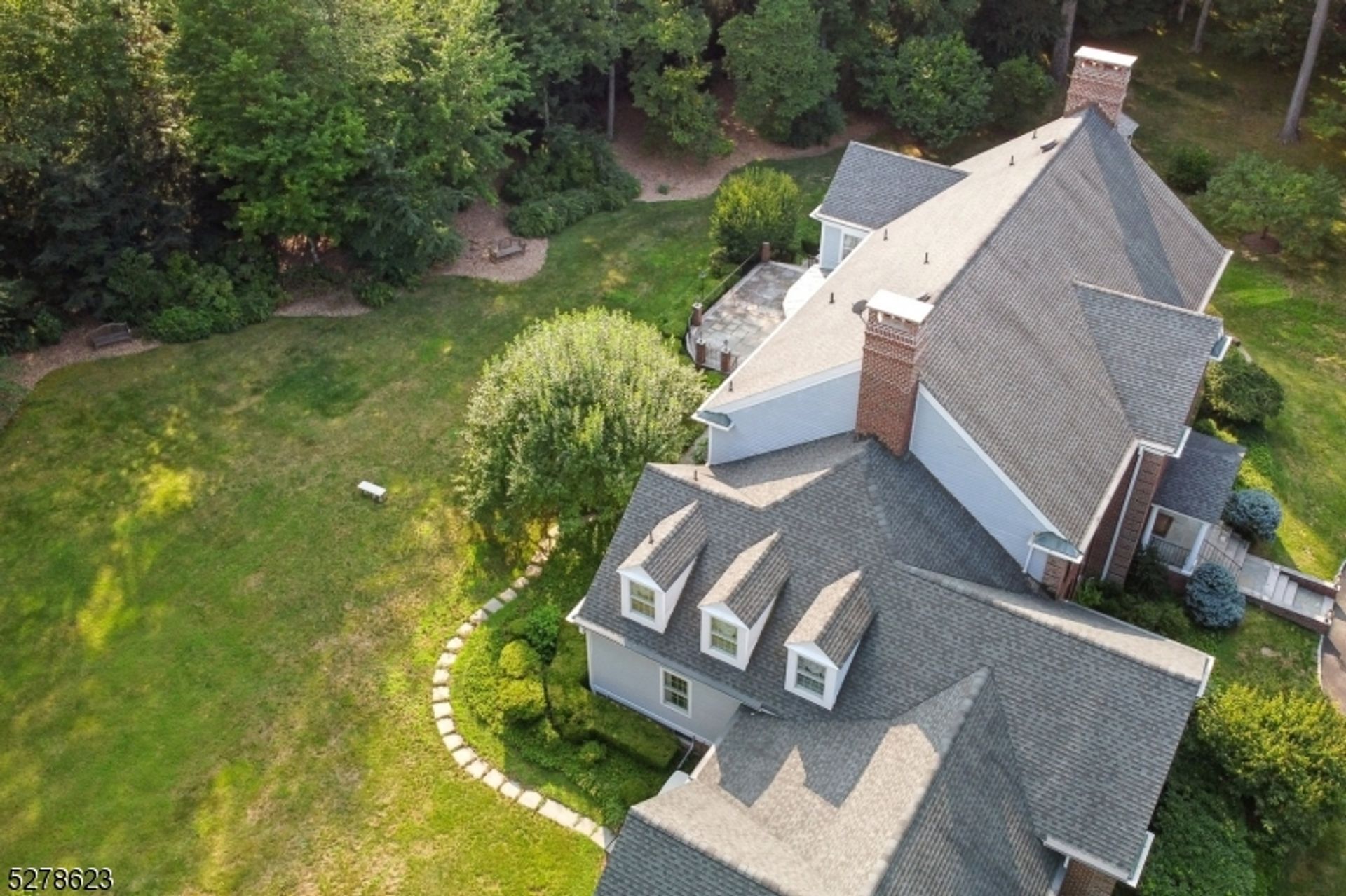 Aerial view showcasing a sprawling backyard with lush greenery and stone pathways.