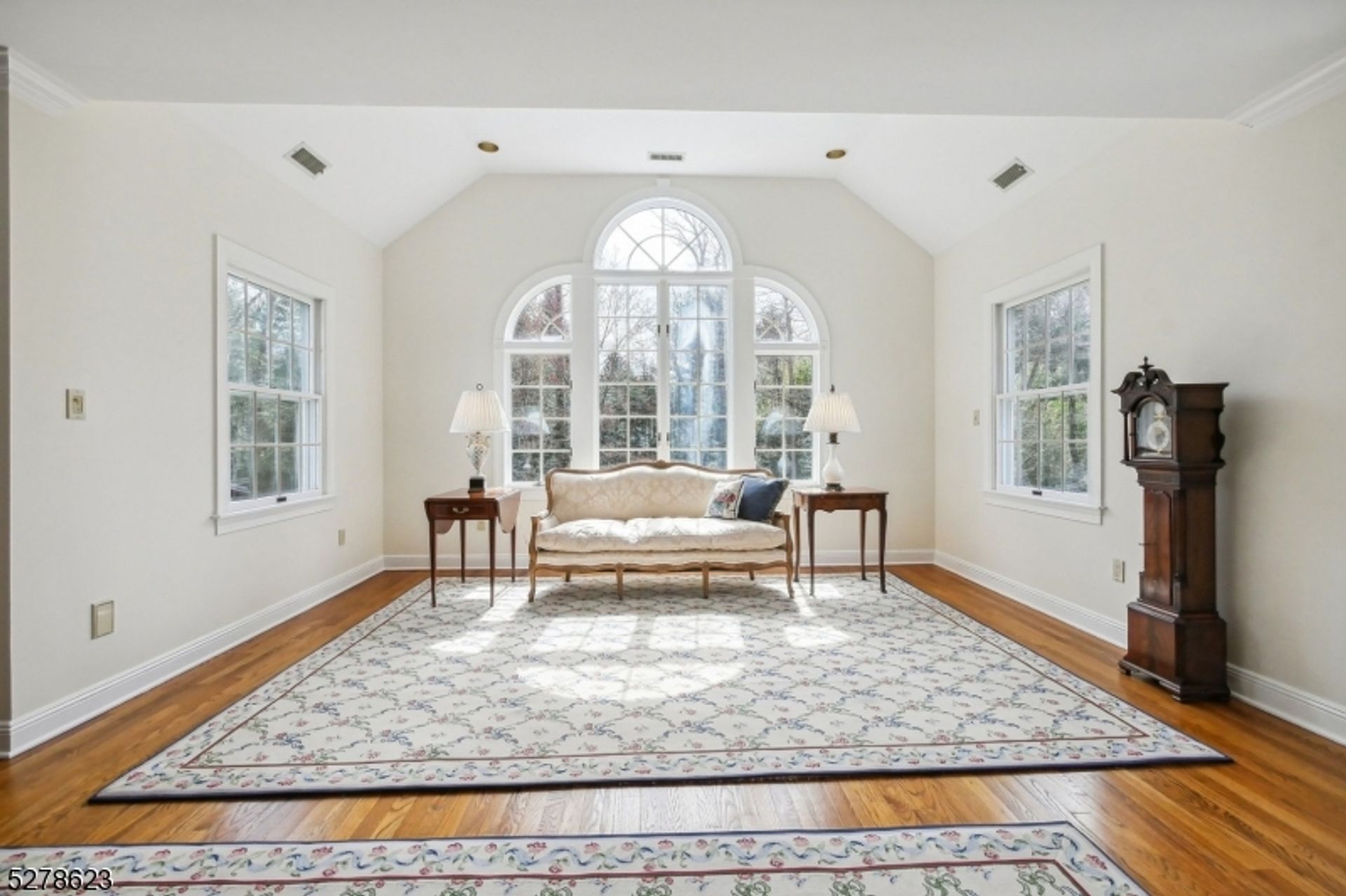 Sunlit sitting area showcases a charming sofa framed by arched windows and polished hardwood floors.