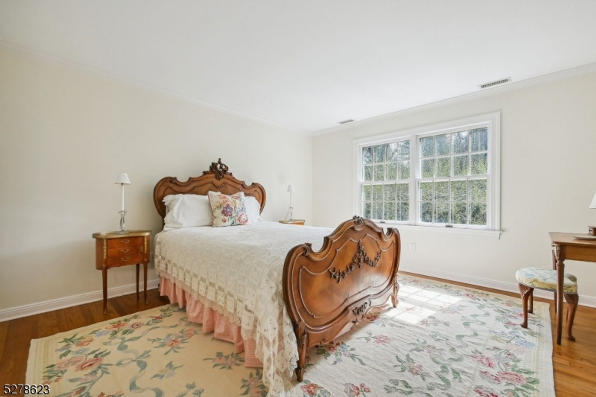 Ornate wooden bed frame with floral detailing stands out against a serene, light-filled bedroom with soft pastel accents.