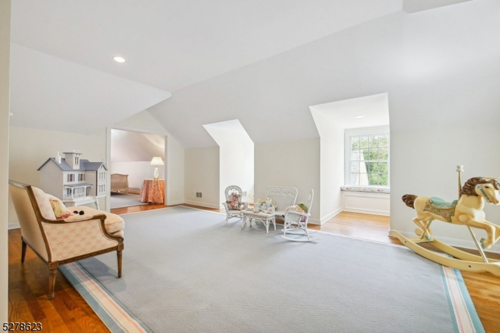 Bright and airy playroom features soft carpet, a charming dollhouse, and a vintage rocking horse, illuminated by natural light from multiple windows.