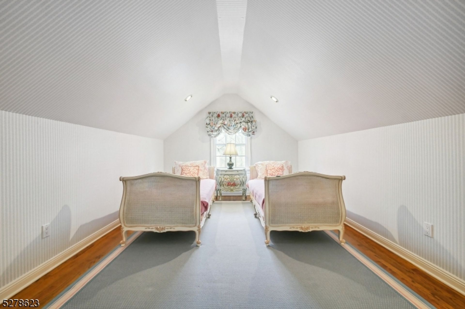 Cozy attic bedroom features twin antique beds, soft pastel decor, and a charming arched window for natural light.