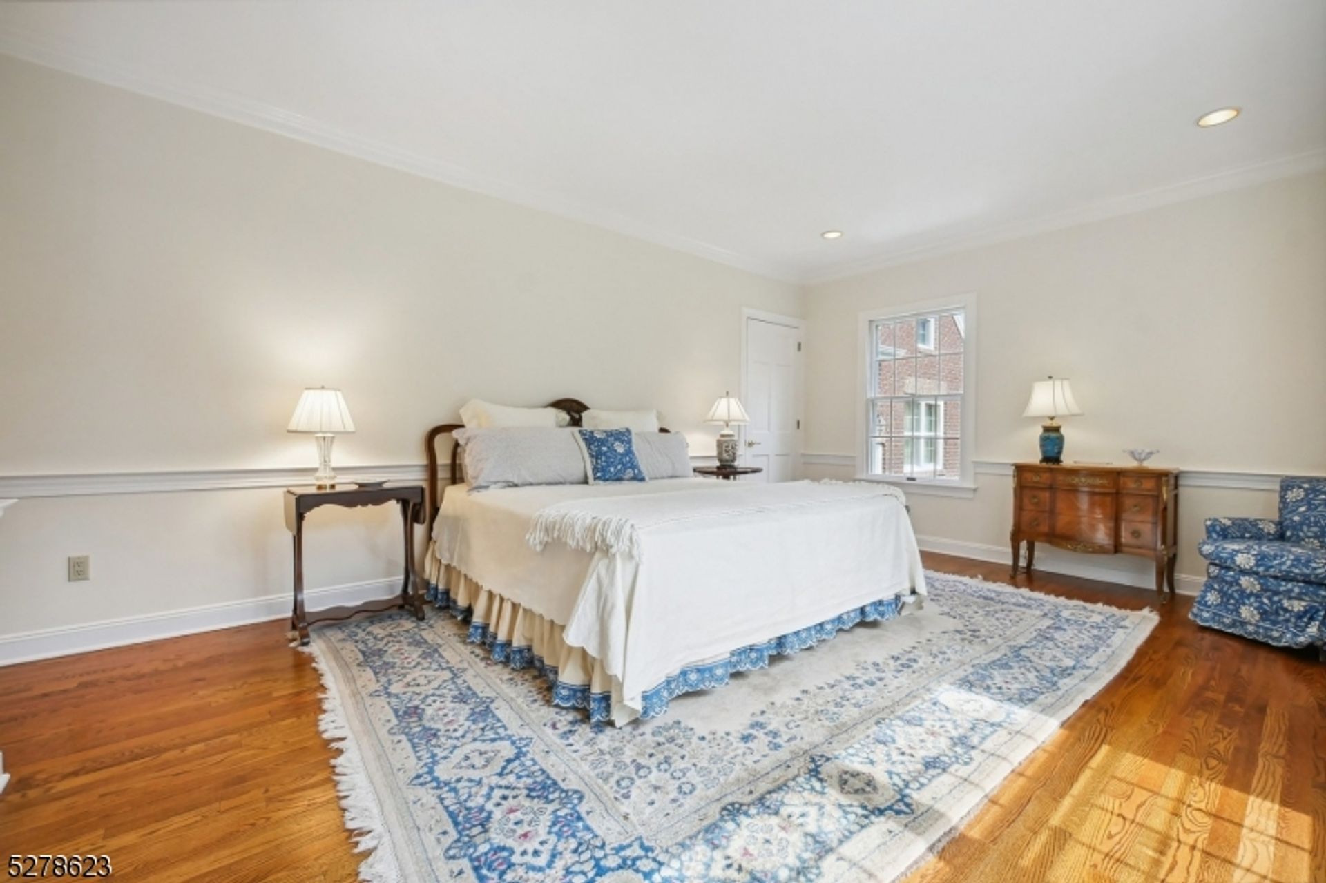 Spacious bedroom showcases a serene color palette with hardwood floors, classic furnishings, and natural light.