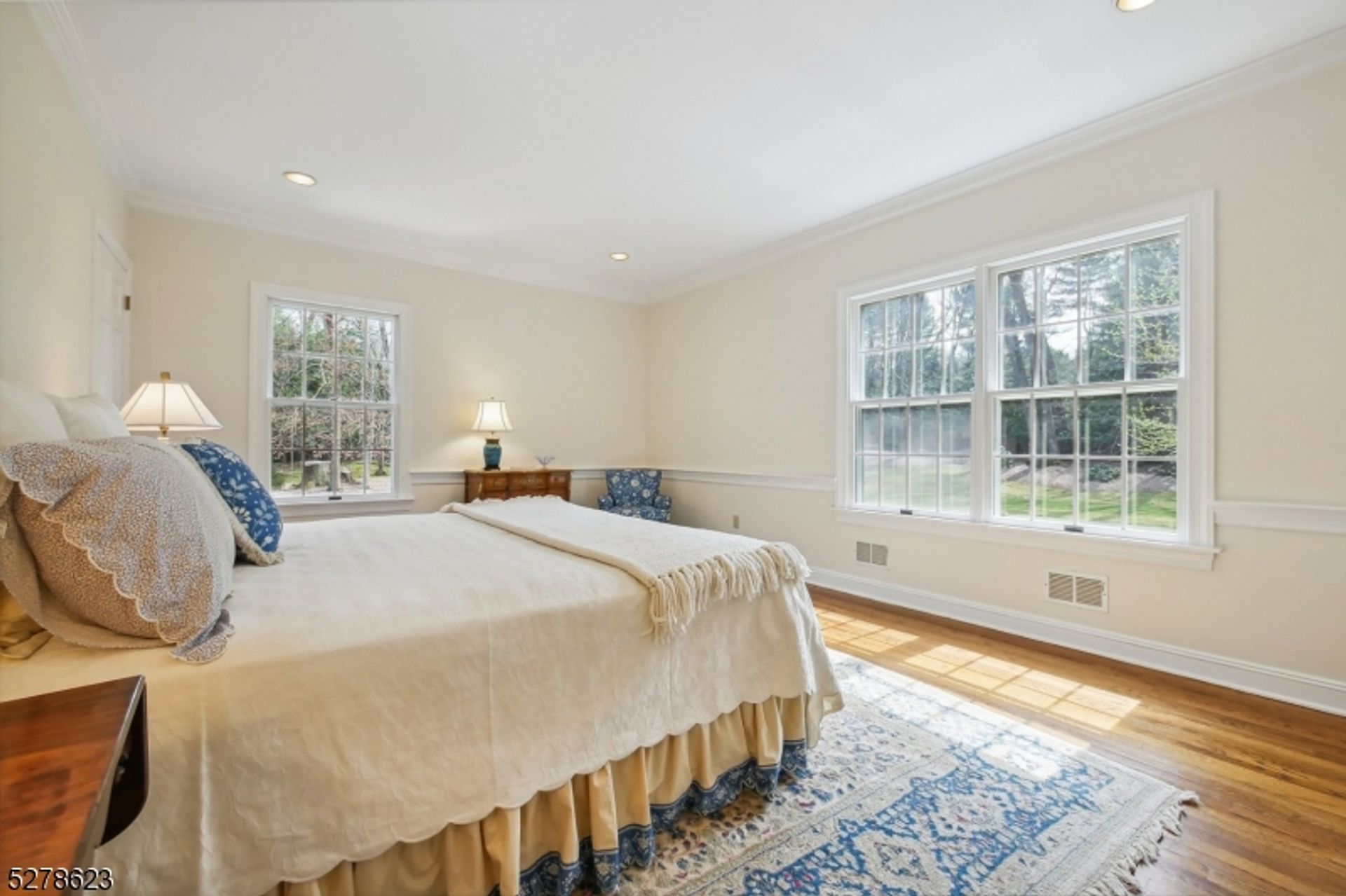 Sunlit bedroom offers peaceful views of the surrounding greenery through large windows.