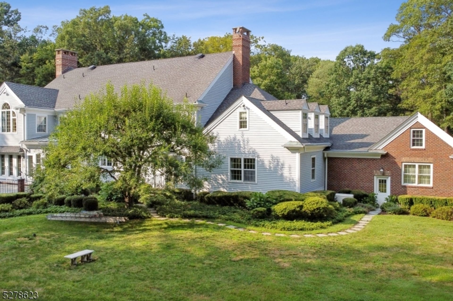 Side view of a classic home with brick and siding, surrounded by landscaped greenery and a stone pathway.