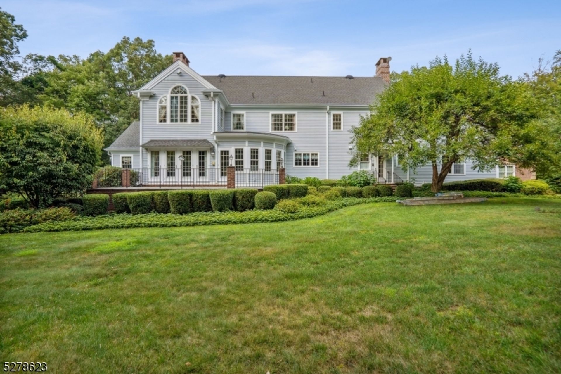 Elegant backyard view featuring manicured landscaping, a spacious lawn, and a grand white exterior with arched windows.