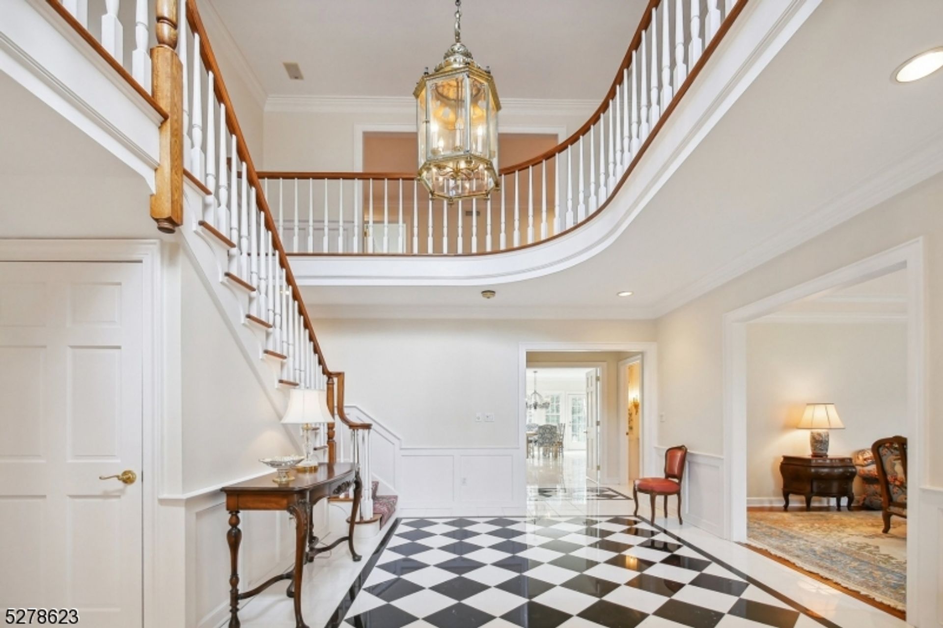 Grand foyer showcasing a sweeping staircase, checkerboard flooring, and a statement chandelier.