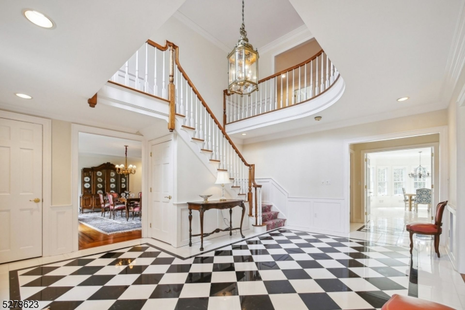 Elegant entryway with striking checkerboard flooring, a curved staircase, and access to the dining room and sunlit living areas.