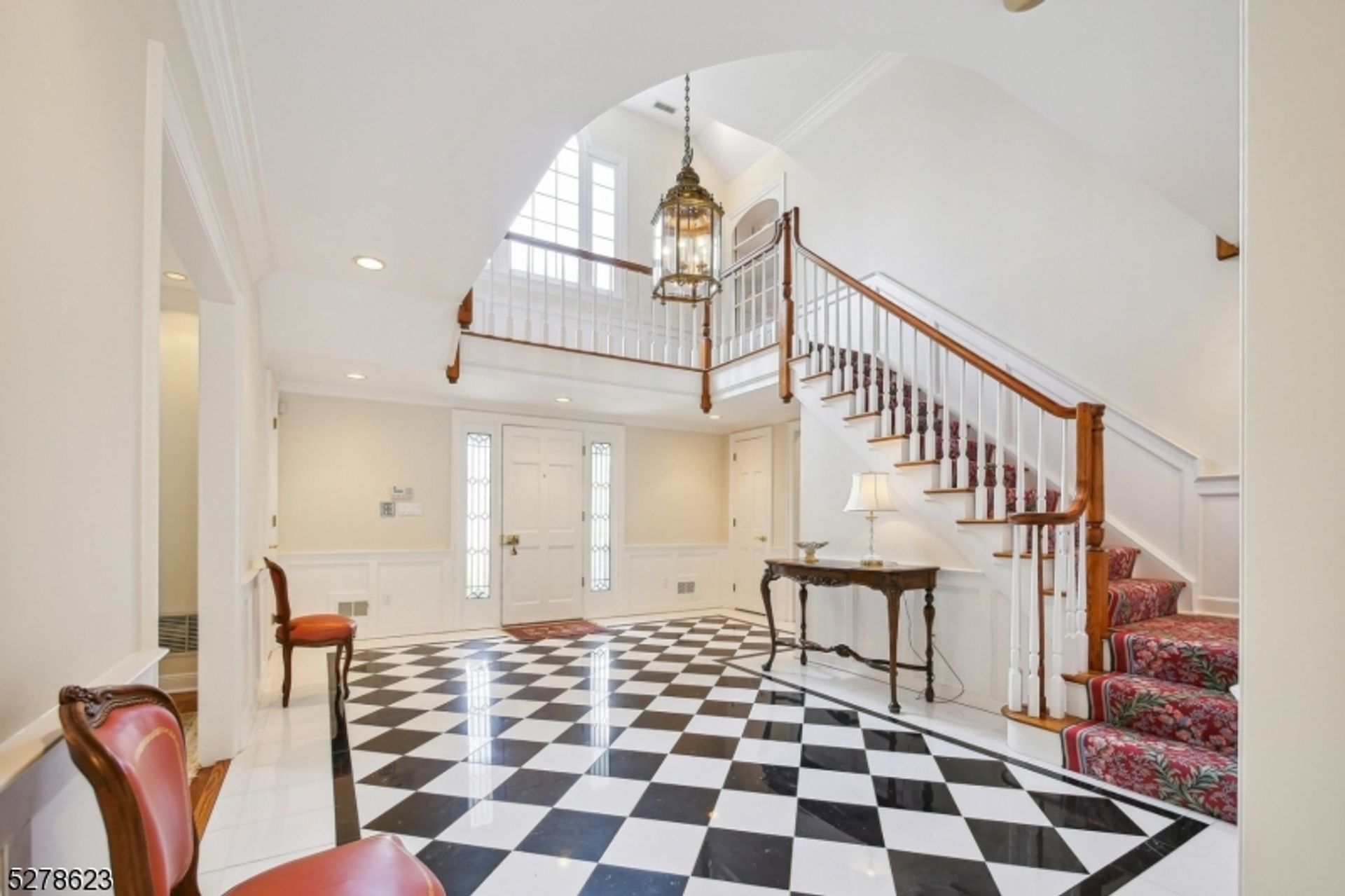 Grand foyer with black-and-white tile flooring, a chandelier, and a sweeping staircase with intricate wooden details.