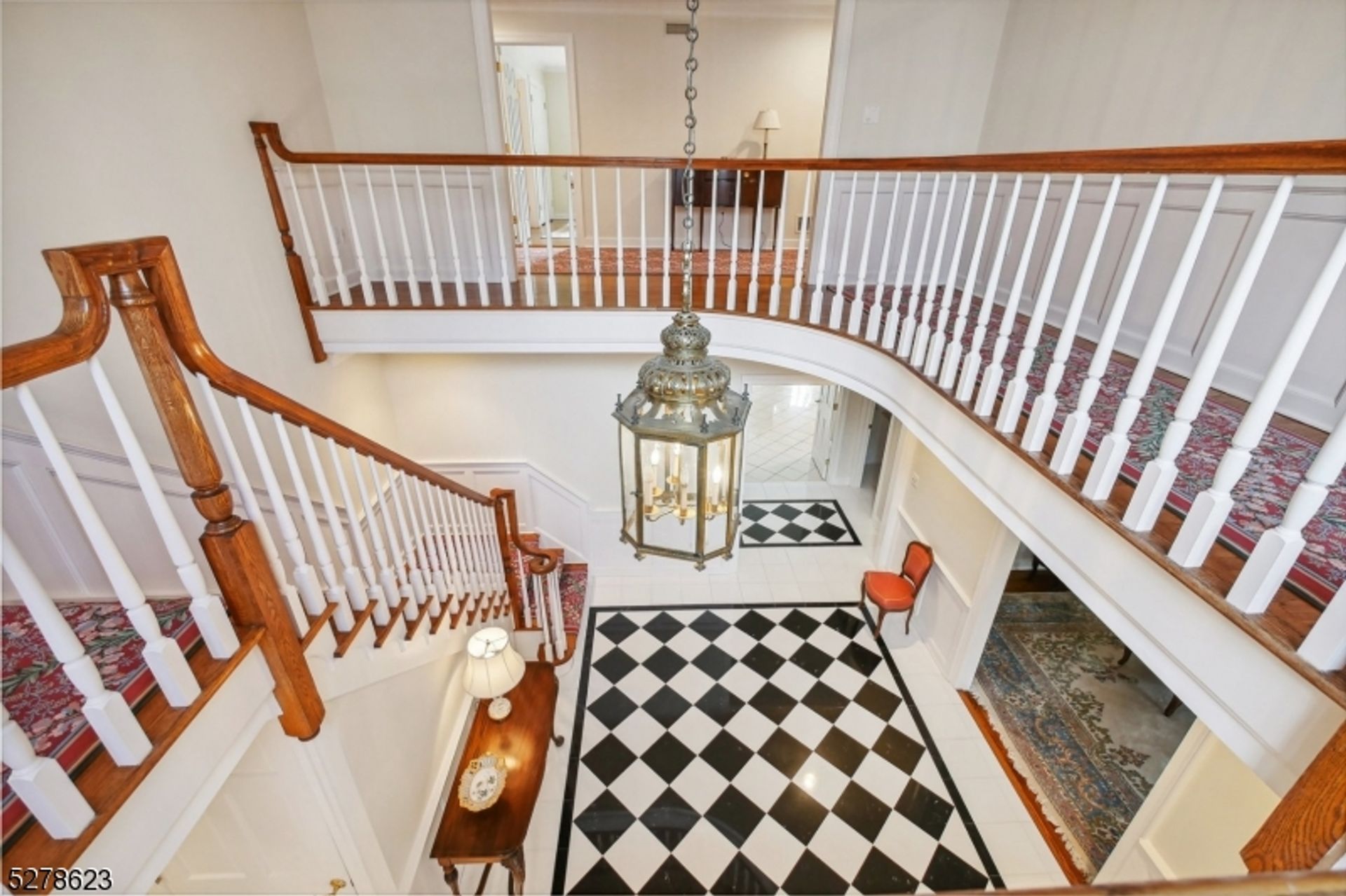 Elegant aerial view of the foyer showcasing the curved staircase, glossy black-and-white tile flooring, and a vintage chandelier.