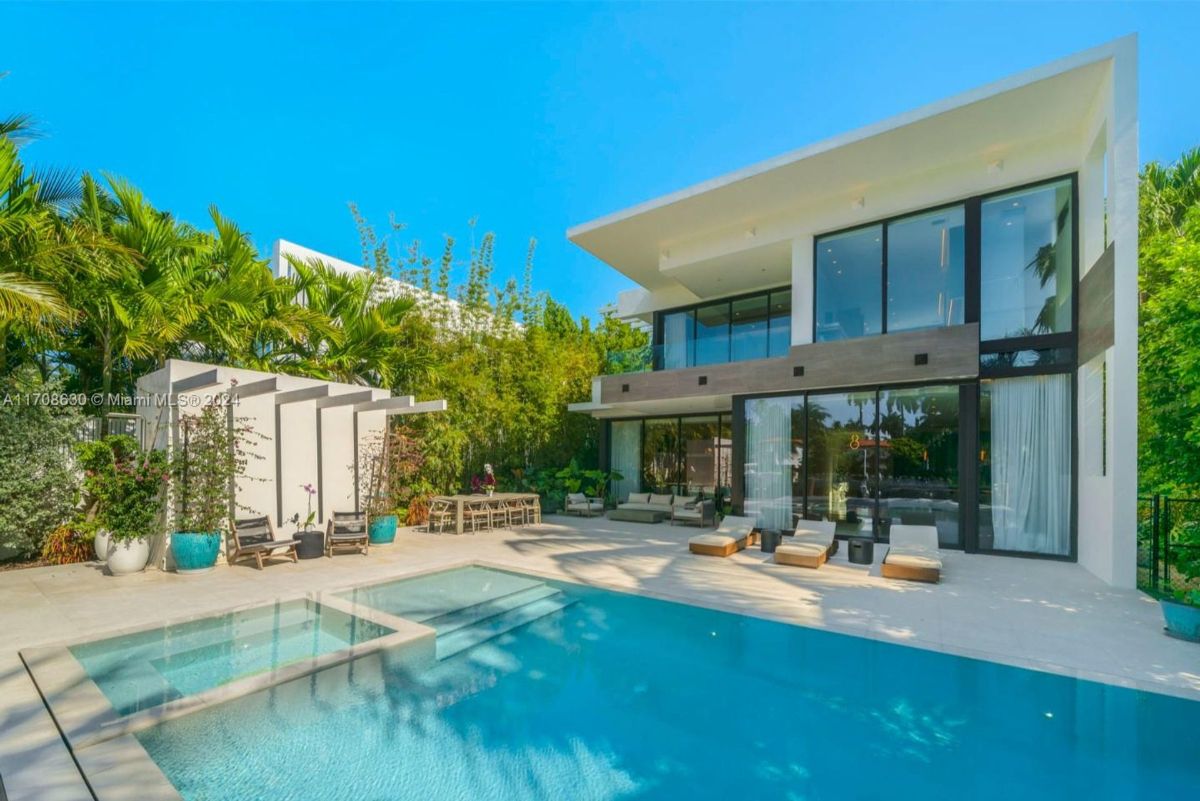 Modern backyard featuring a sleek pool, outdoor lounge area, and lush tropical landscaping.